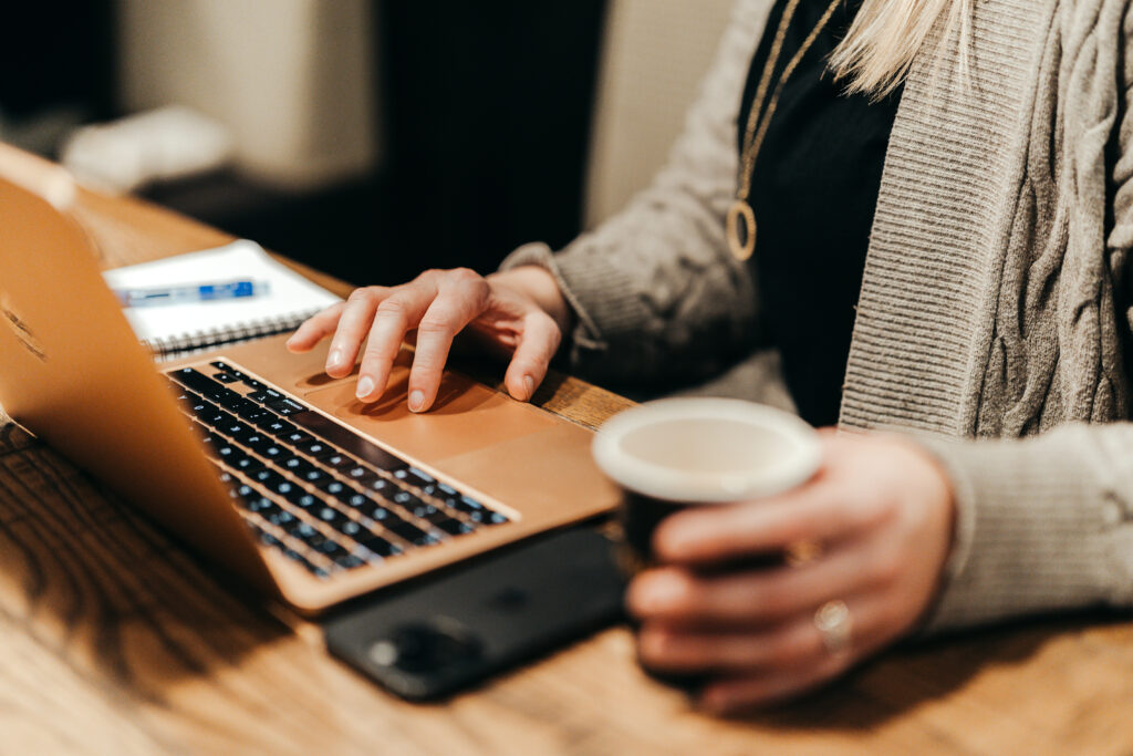 Kuvassa ulkoistettu markkinointipäällikkö työskentelee tietokoneella, kahvikuppi kädessään