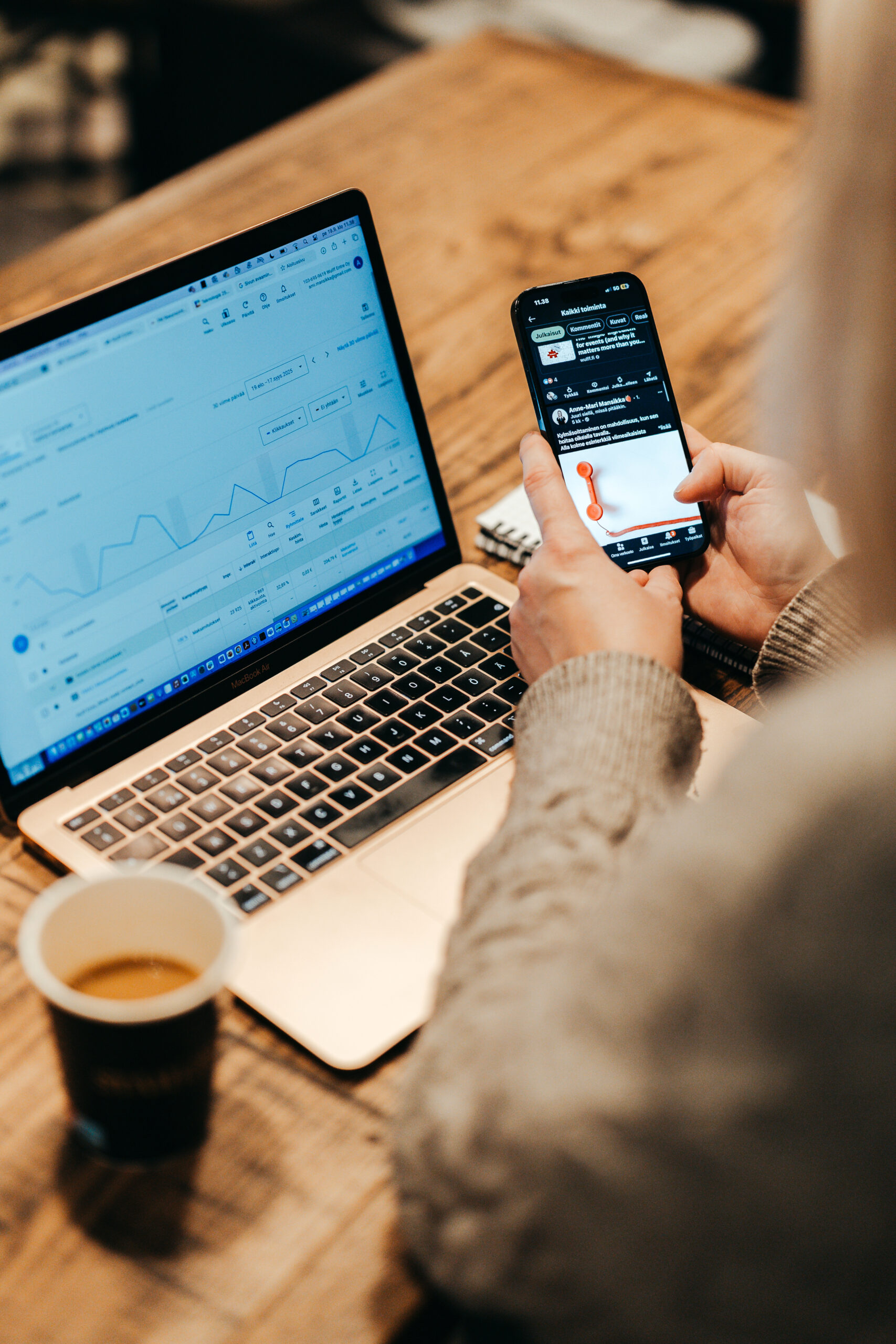 Markkinoinnin asiantuntija analysoimassa verkkosivujen ja somen dataa kannettavan tietokoneen ja puhelimen avulla, tarjoten markkinoinnin tukea aloitteleville yrittäjille